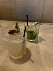 two handmade margaritas sitting on a table with garnishes on the rims of the drinks